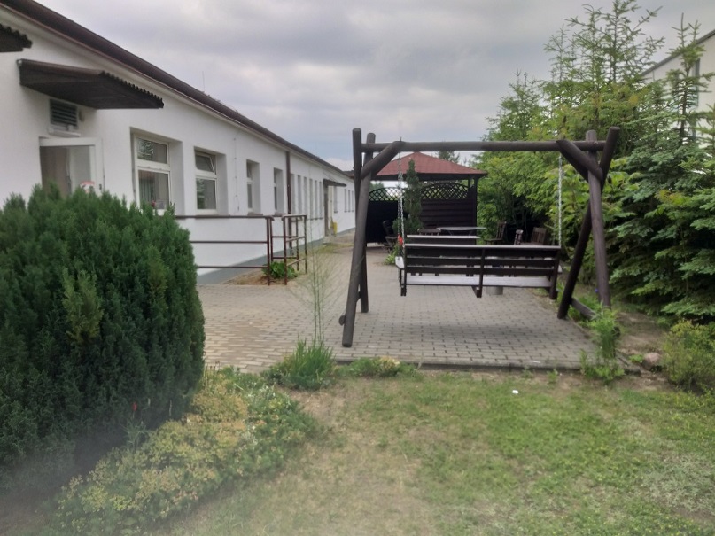 Zdjęcie terenu Centrum Leczenia Nerwic Mawiko, ośrodka specjalizującego się w terapii zaburzeń lękowych i nerwicowych. Przedstawia część rekreacyjną z drewnianą huśtawką, altaną oraz stołem z ławkami, otoczoną zielenią. Spokojne, zielone otoczenie sprzyja relaksacji i wspiera proces terapeutyczny pacjentów